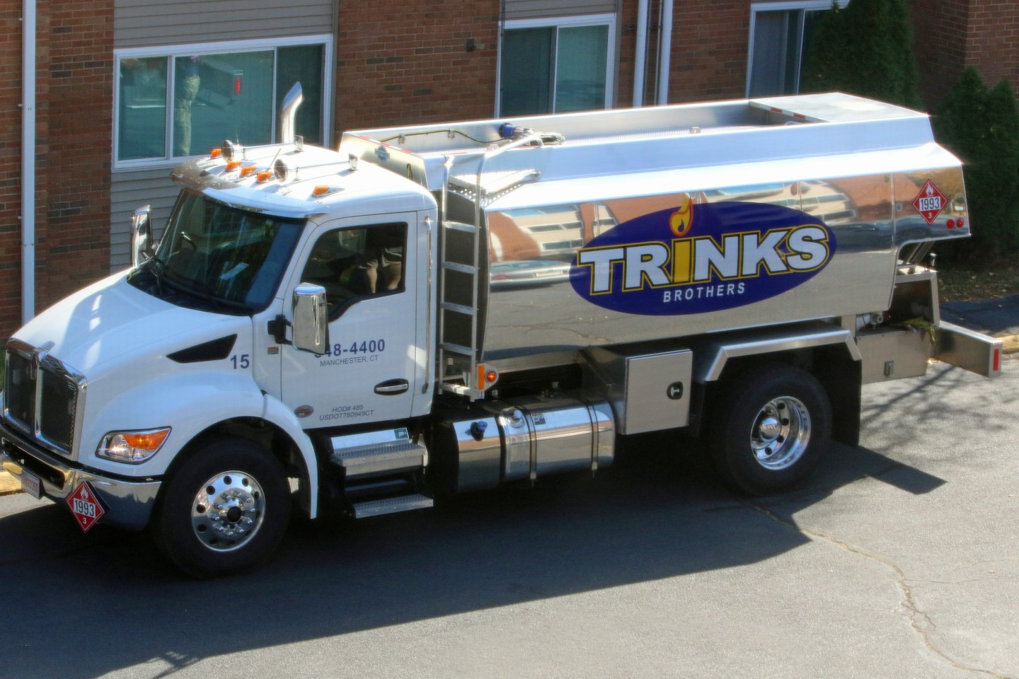 White tanker truck parked beside a brick and siding building.