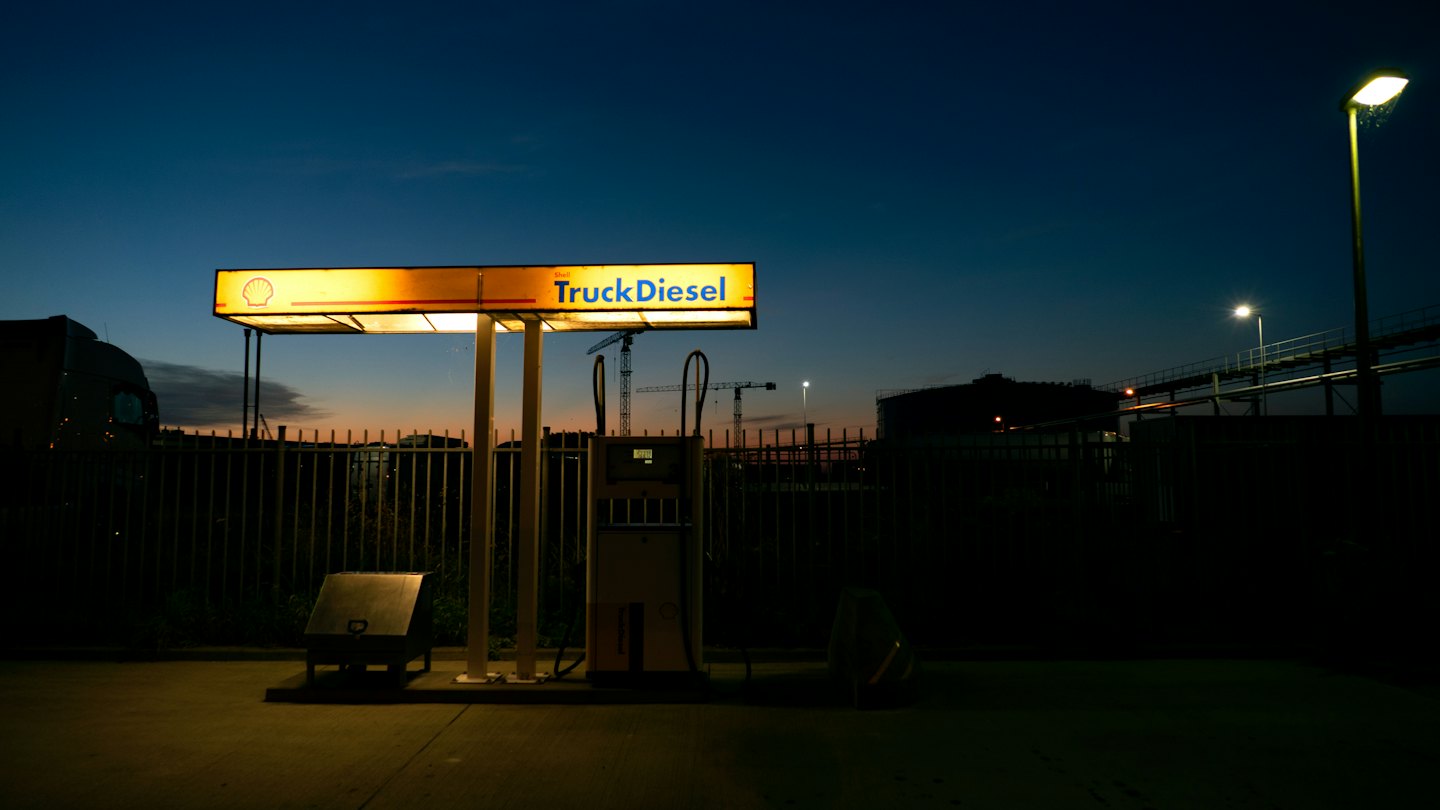 Illuminated diesel fuel pump stands in an industrial truck yard.
